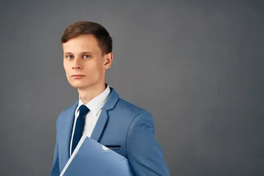 Молодой человек в голубом пиджаке с папкой на сером фоне