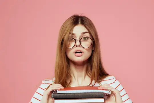 Молодая студентка с книгами на розовом фоне, в очках
