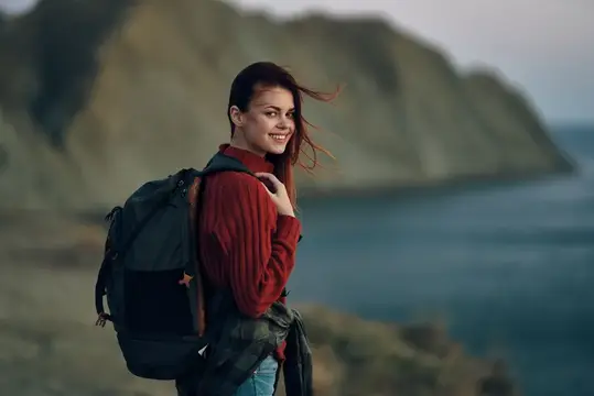 Улыбающаяся девушка с рюкзаком на фоне гор и моря