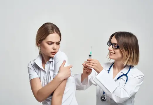 Врач в очках готовится сделать укол в плечо пациентке