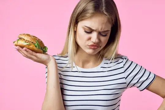 Весёлая женщина с фастфудом в руках, закуски выглядят аппетитно на розовом фоне