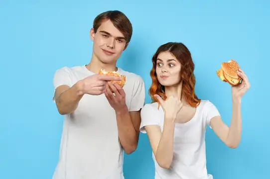 Молодые парень и девушка с бургерами на голубом фоне