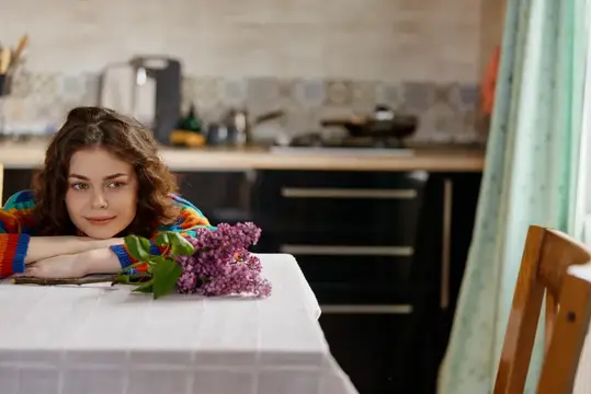 Молодая женщина с букетом сирени за столом на кухне