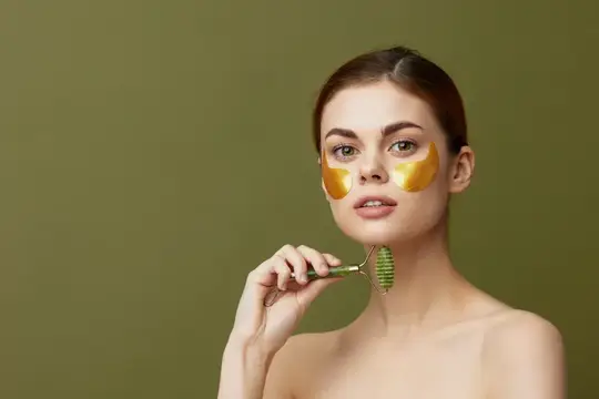 Молодая женщина с массажёром для лица, золотые патчи на лице, крупный план, образ жизни