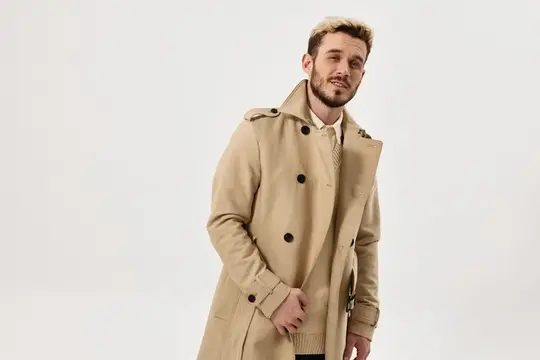Молодой мужчина с бородой в бежевом пальто на светлом фоне