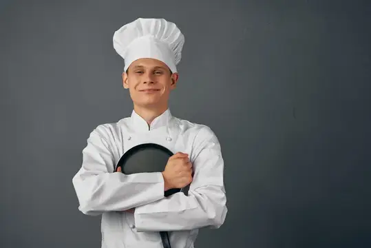 В кафе повар в униформе держит сковороду в руках и занимается приготовлением пищи в ресторане