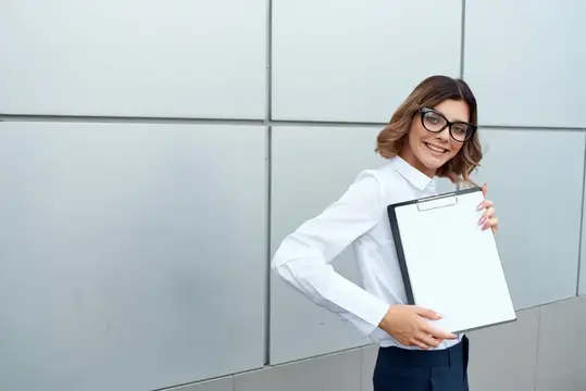 Улыбчивая девушка в очках с планшетом у серой стены