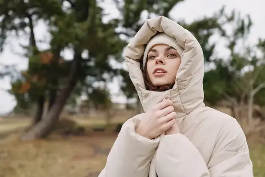 Молодая женщина в светлом пуховике с капюшоном на осенней прогулке