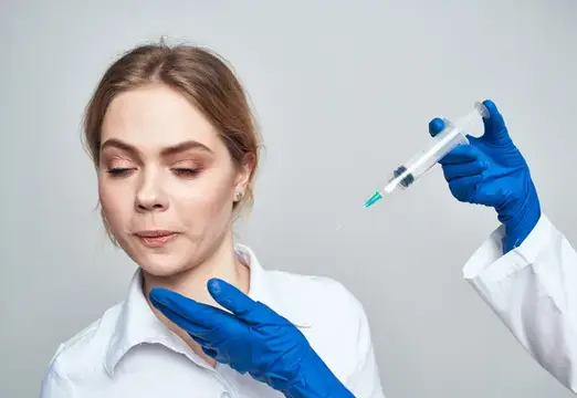 Косметолог в синих перчатках готовит инъекцию молодой женщине