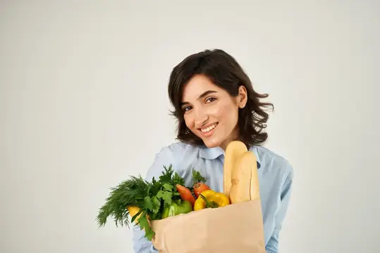 Симпатичная женщина с сумкой продуктов и овощей на светлом фоне, олицетворяющая здоровое питание