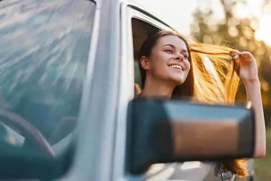 Улыбающаяся девушка высунулась из окна автомобиля на закате