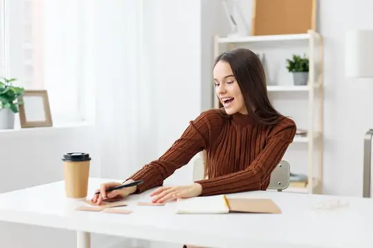 Улыбающаяся темноволосая женщина работает за белым столом у окна