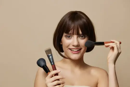 Улыбающаяся шатенка с короткой стрижкой держит кисти для макияжа