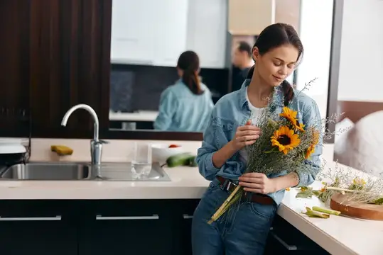 Молодая женщина с букетом подсолнухов стоит на кухне