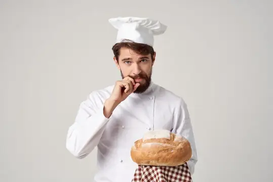Задумчивый бородатый пекарь в колпаке с хлебом
