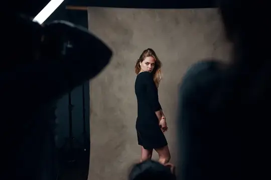 Молодая женщина в черном платье позирует на фоне фотозоны в студии