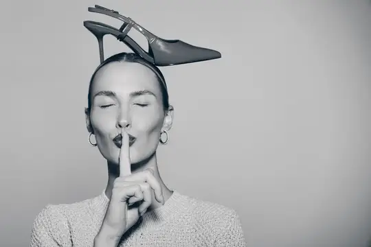 Девушка с туфлей на голове прикладывает палец к губам