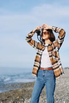 Девушка в клетчатой рубашке фотографирует на плёночный фотоаппарат у моря