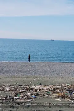 Одинокий человек стоит на галечном берегу среди мусора