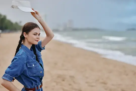 Молодая женщина в джинсовом платье с козырьком на пустынном пляже