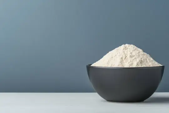 Пшеничная мука горкой в тёмной миске на сером фоне