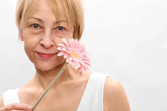 Улыбающаяся блондинка держит розовую герберу у лица