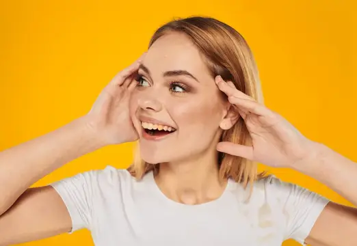 Светловолосая девушка в белой футболке улыбается на жёлтом фоне
