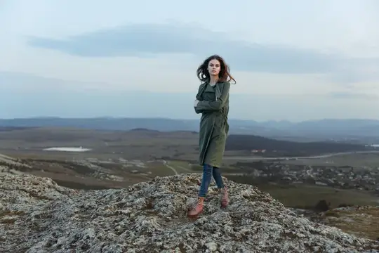 Девушка в зелёном плаще стоит на скалистой вершине над долиной