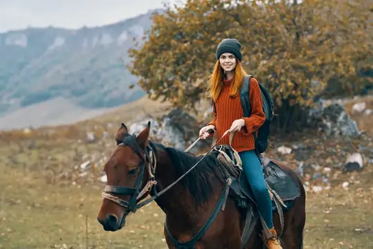 Женщина-туристка с рюкзаком едет верхом на лошади в горах, путешествуя на природе