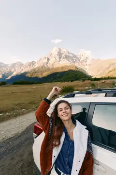 Улыбающаяся девушка у внедорожника на фоне гор