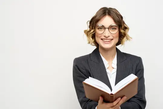 Женщина на работе с книгой в руке на светлом фоне, в классическом костюме и очках
