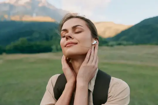 Молодая женщина с закрытыми глазами слушает музыку в наушниках на фоне гор