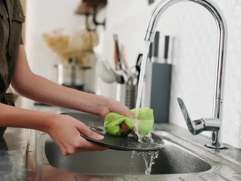 Женщина моет тёмную тарелку под струёй воды на кухне
