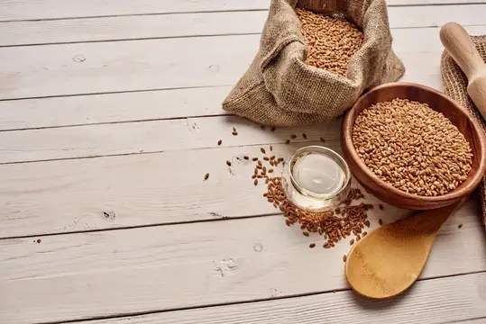 Мешок и миска с пшеничными зёрнами на светлом деревянном столе