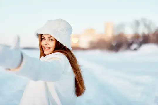 Улыбающаяся девушка в белой панаме и пуховике на зимней прогулке