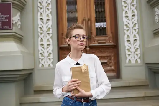 Коротко стриженная женщина в очках прогуливается по городу с книгой в руках