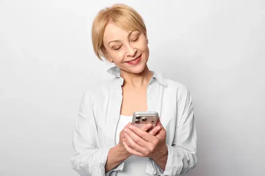 Пожилая женщина использует смартфон для технологий и общения, социальная связь с улыбкой, студийный фон, цифровой экран в фокусе, концепция повседневной современной жизни