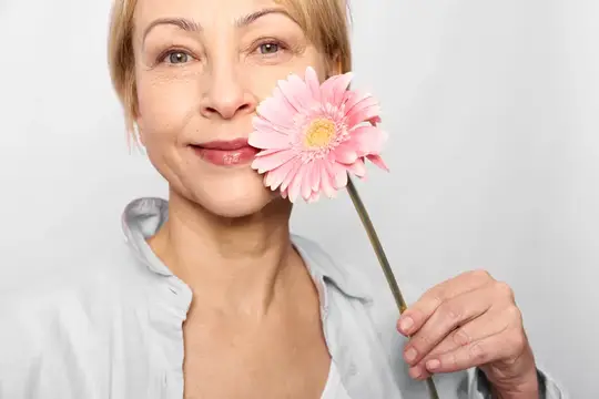 Улыбающаяся женщина держит розовую герберу у лица