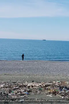 Одинокий человек стоит на галечном пляже среди мусора у моря