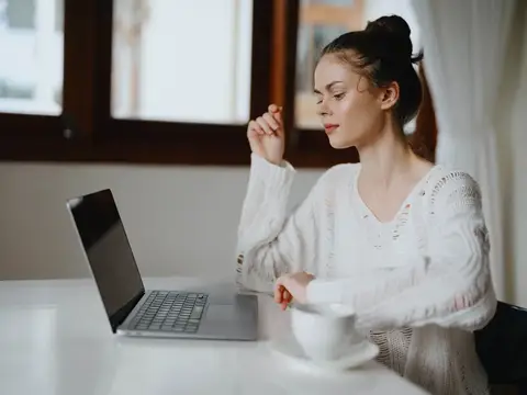 Творческая молодая женщина работает за письменным столом дома в уютном интерьере с чашкой напитка