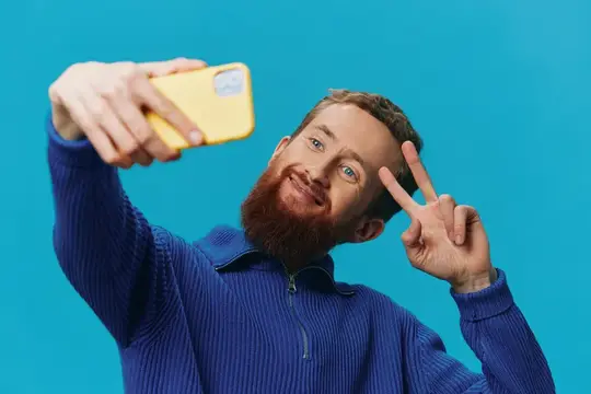 Рыжебородый мужчина делает селфи с желтым телефоном на синем фоне