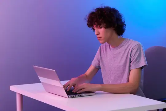 Кудрявый парень в футболке работает за ноутбуком в неоновом свете