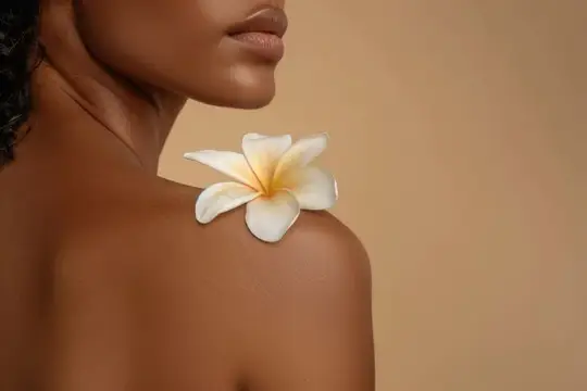 Темнокожая женщина с белым цветком на плече на бежевом фоне