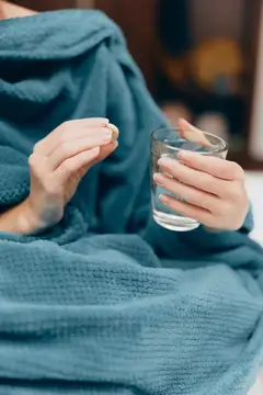 Женщина в махровом халате держит стакан воды и таблетку