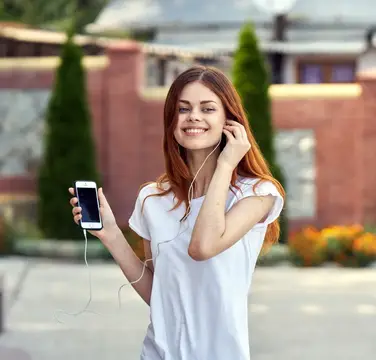 Привлекательная женщина с телефоном в руках на улице, в наушниках
