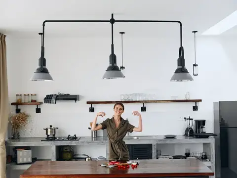 Улыбающаяся женщина показывает мускулы на кухне с чёрными лампами