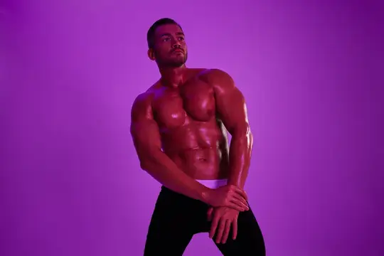 Мускулистый темноволосый мужчина позирует на фиолетовом фоне