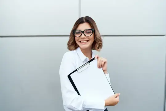 Улыбчивая деловая женщина с документами стоит возле здания, она выглядит профессионально