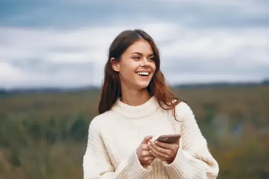 Улыбающаяся темноволосая девушка со смартфоном на фоне поля
