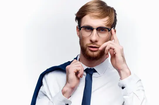 Рыжебородый мужчина в очках поправляет галстук на белом фоне